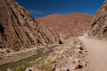 Explore and adventure. Traveling along the dirt road high in the mountains. View of the route across the arid desert besides the river flowing along the rocky mountains. 