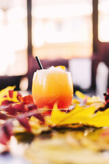Orange cocktail in a restaurant on a table with colorful autumn leaves side view