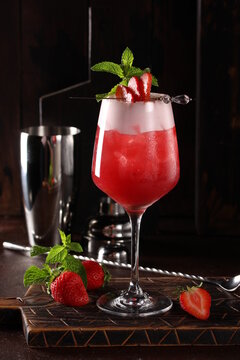 Alcoholic cocktail. Strawberry fizz. Red drink of gin, lime, cranberry, protein with mint in a clear glass on a wooden board on a brown table. Bar menu. Background image, copy space, vertical