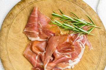 Crudo ham with rosemary sprigs on rustic wooden board - top view