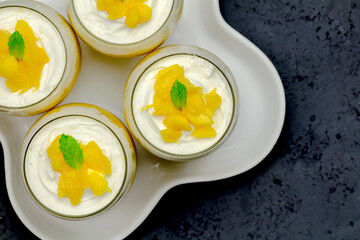 Mango syllabub desserts with cardamom spiced cream in glasses with mint sprigs - top view