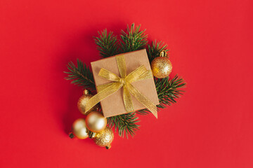 Gift box with spruce branches and golden balls on a red background.