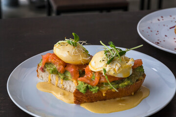Restaurant food and some plates of breakfast toasts with salmon, guacamole, poached egg, with sauce. Fresh food close-up