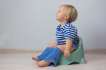 Naklejka premium small Caucasian boy with blond hair and blue eyes is sitting on a child's toilet