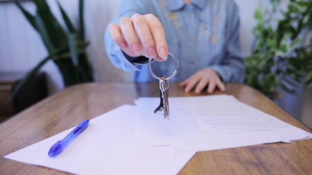 A woman takes the keys and shows them in close-up. Table with papers and hand close-up. Indoors. The concept of leasing