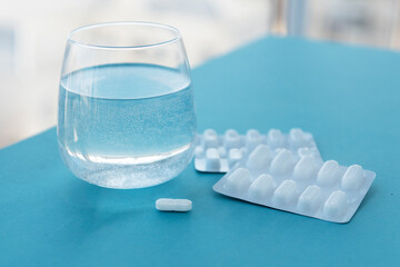transpatent glass with pure water and white pills on blue table in hospital, copy space for text. Treatment from headaches, flu, influenza, viruses. Healthcare concept