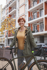 Vertical portrait of a happy young woman laughing, standing on city street with a bicycle