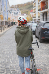 Rear view vertical shot of a woman in protective cycling helmet walking on the road with her bicycle