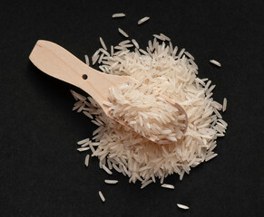 Heap of wite basmati rice with wooden scoop on black background.  Flat lay.