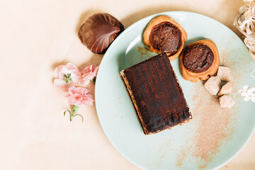 A piece of tiramisu tart in a green plate. Zephyr with chocolate and small pink carnations