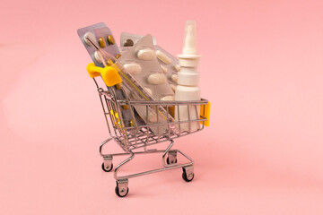 Shopping grocery cart with medicament, tablet, spray, thermometer on pink background. Concept of healthy care, business, shopping, sales.