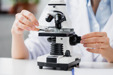 cropped of female scientist holding glass test plate near microscope in lab