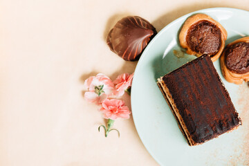 A piece of tiramisu tart in a green plate. Zephyr with chocolate and small pink carnations