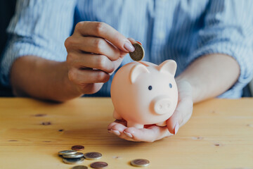 the woman's hand puts a coin in a pink piggy bank standing on the table. Concept of saving money or savings, investment during the global crisis