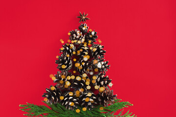 Christmas tree made of cones on red background. Holiday greeting card. Top view. Copy space.Christmas or New Year flatlay.