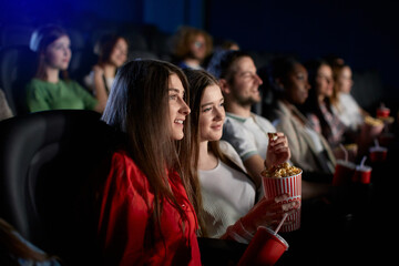 Young girls enjoying free time in movie theater. - obrazy, fototapety, plakaty
