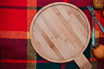 Background for cooking or baking on cold seasons: round empty wooden bamboo cutting board on checkered cloth with fruits