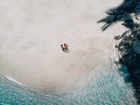 Beach drone view Phuket tropical island, white beach with waves, couple lay down on the beach man and woman. Aerial Photo. Trip to warm destination.