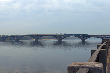 Fototapeta premium Scenic morning landscape view Dnieper River. Metro (Subway) Bridge over Dnipro River. The metro train moves on the bridge. Nature landscape with autumn colors. Kyiv, Ukraine