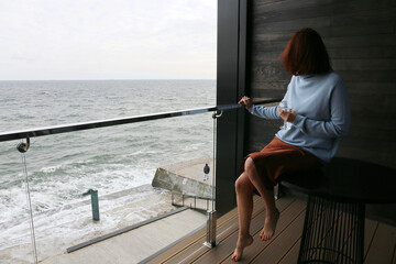 woman in silk dress and blue sweater with glass on the balcony by the sea