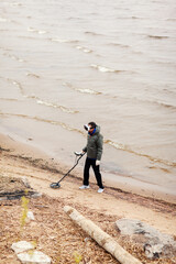 From above view of young man in VR headset with metal detector searching for treasures on sea coast