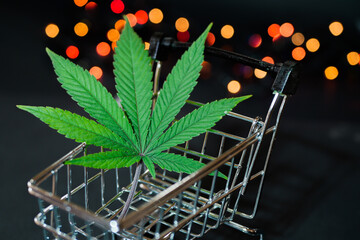 Cannabis leaf in shopping cart close up. Christmas lights. Black friday sale. Marijuana delivery 