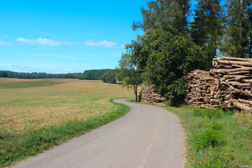 Beautiful panoramic view over a small French country road with extensive fields and packed trees to the side on a summer day.