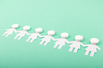 A chain of paper people with pills on a green background. Medicine concept.