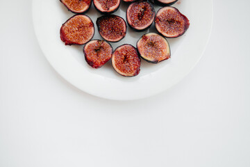 Ripe and sweet figs cut and arranged in a plate on a white background with free space. Fruits and vegetarianism