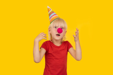 Surprised boy in clown outfit on yellow background. Childrens holiday