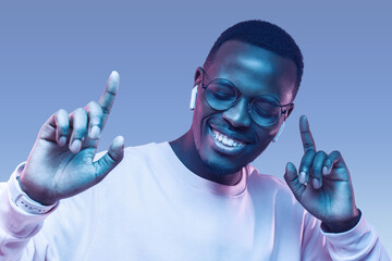 Portrait of happy young african man listening to music with wireless earphones isolated on blue background