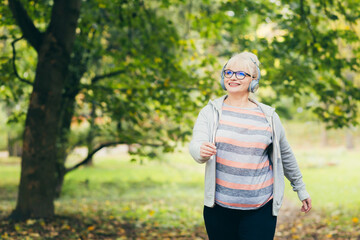Beautiful senior woman in a backpack on a walk in the park, listening to music with headphones