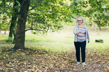 Beautiful senior woman in a backpack on a walk in the park, listening to music with headphones