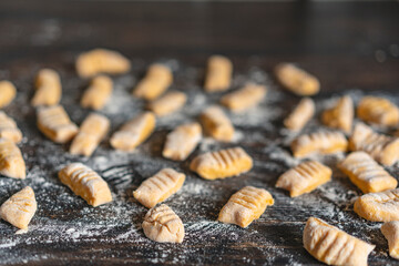Hand made raw gnocchi di patata,traditional Italian potato noodles ready for cooking on wooden table. Selective focus, close up view, copy space. Vegan food. Process of cooking.