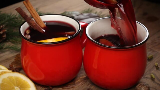 Pouring of red cup with mulled wine on festive table, decorated with fir branch, slices of tangerine and anise star, slow motion