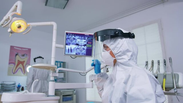 Patient pov looking at dentist in ppe suit showing x-ray image in dental office. Stomatology specialist wearing protective hazmat suit against coroanvirus showing radiography in clinic with new normal