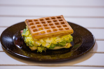 Waffle de palta y huevo fresco emplatado en plato negro desgastado