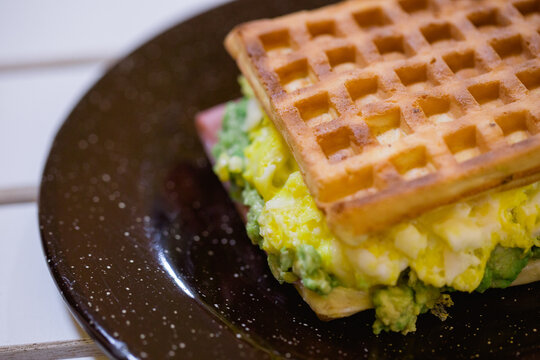 Waffle de palta y huevo fresco emplatado en plato negro desgastado