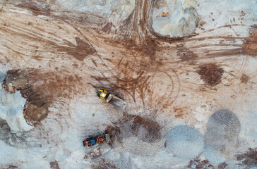 Heavy machines, including yellow trucks, in the working environment in a mine, seen in an aerial photo taken from a drone
