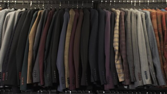 Camera shows colorful male suits in row in a hanger. Shop jacket men series, business hanger clothing 4k