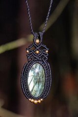 Mineral labradorite gemstone ornamental pendant on blury forest background