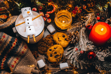 Christmas food white cup with hot chocolate snowman marshmallows. homemade cookie, cinnamon sticks fir xmas tree branches with warm garland lights. New year celebration. Festive dessert breakfast idea