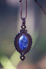 Mineral lapis lazuli gemstone ornamental pendant on blury forest background