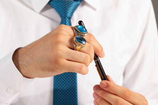 Blue silver rings and accessories on male finger with blue tie in white shirt.