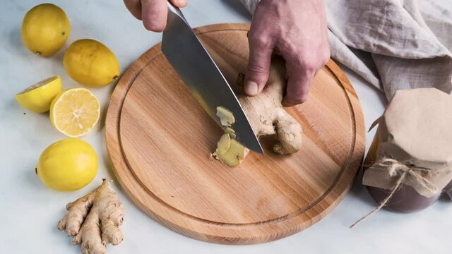 Men hands cut with a knife ginger root on wooden cutting board for homemade drink from lemons, honey, fresh ginger root and hot water.