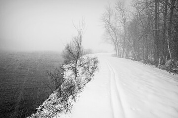 Winter scene on empty pathway along river, snow and fog, cross country ski tracks in foreground nobody