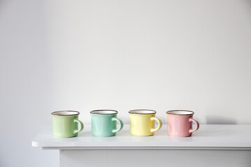 Four small multicolored pastel coffee cups on a white console against a wall background