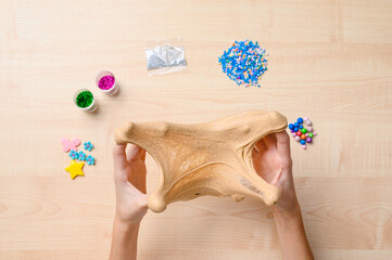 Slime toy in the hands of a child. In the background there is a table and ingredients for...