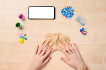 Making slime using the Internet. Children's hands on the table and slime. Next to a smartphone with a blank white display.