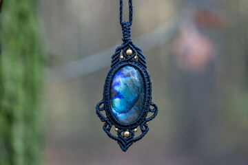 Mineral labradorite gemstone ornamental pendant on blury forest background